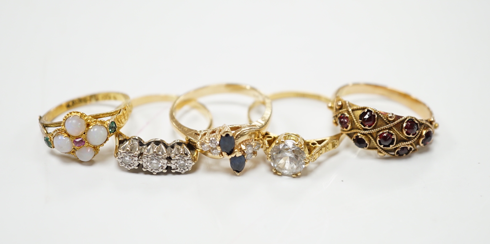 An Edwardian 15ct?, white opal, emerald and amethyst cluster set ring, in the Suffragette colours, size F, together with four other yellow metal and gem set rings including three stone illusion set diamond and a 14k sapp